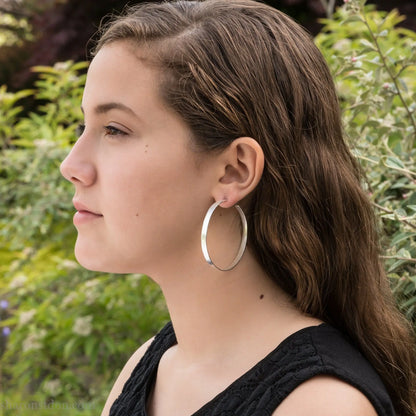 55mm sterling silver hoop earrings with hammered texture and matte brushed finish, shown worn on ear.