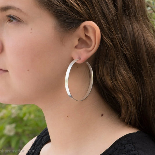55mm sterling silver hoop earrings with hammered texture and matte brushed finish, shown worn on ear.