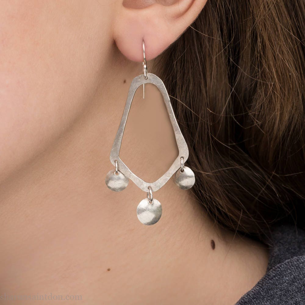 925 sterling silver handcrafted earrings. A hammered, angular, teardrop loop with three dots hanging from the angled teardrop points. Size: 60mm high to top of hook x 35mm at widest point, dots approximately 1cm. Comfortable, lightweight, with handmade ear wire hooks. Worn by a young woman with fair skin and light brown hair.