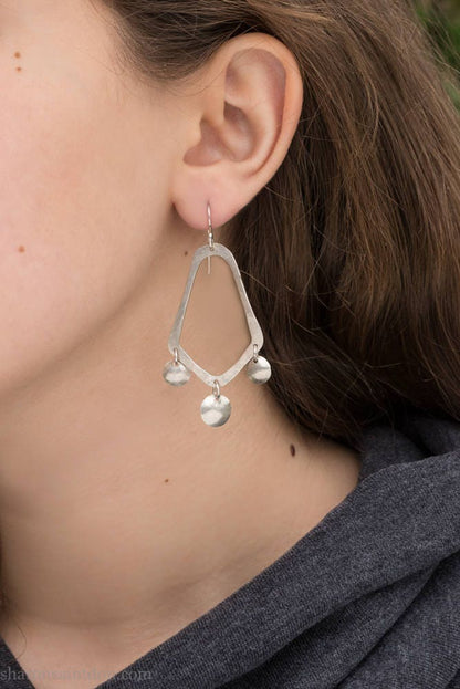925 sterling silver handcrafted earrings. A hammered, angular, teardrop loop with three dots hanging from the angled teardrop points. Size: 60mm high to top of hook x 35mm at widest point, dots approximately 1cm. Comfortable, lightweight, with handmade ear wire hooks. Worn by a young woman with fair skin and light brown hair.