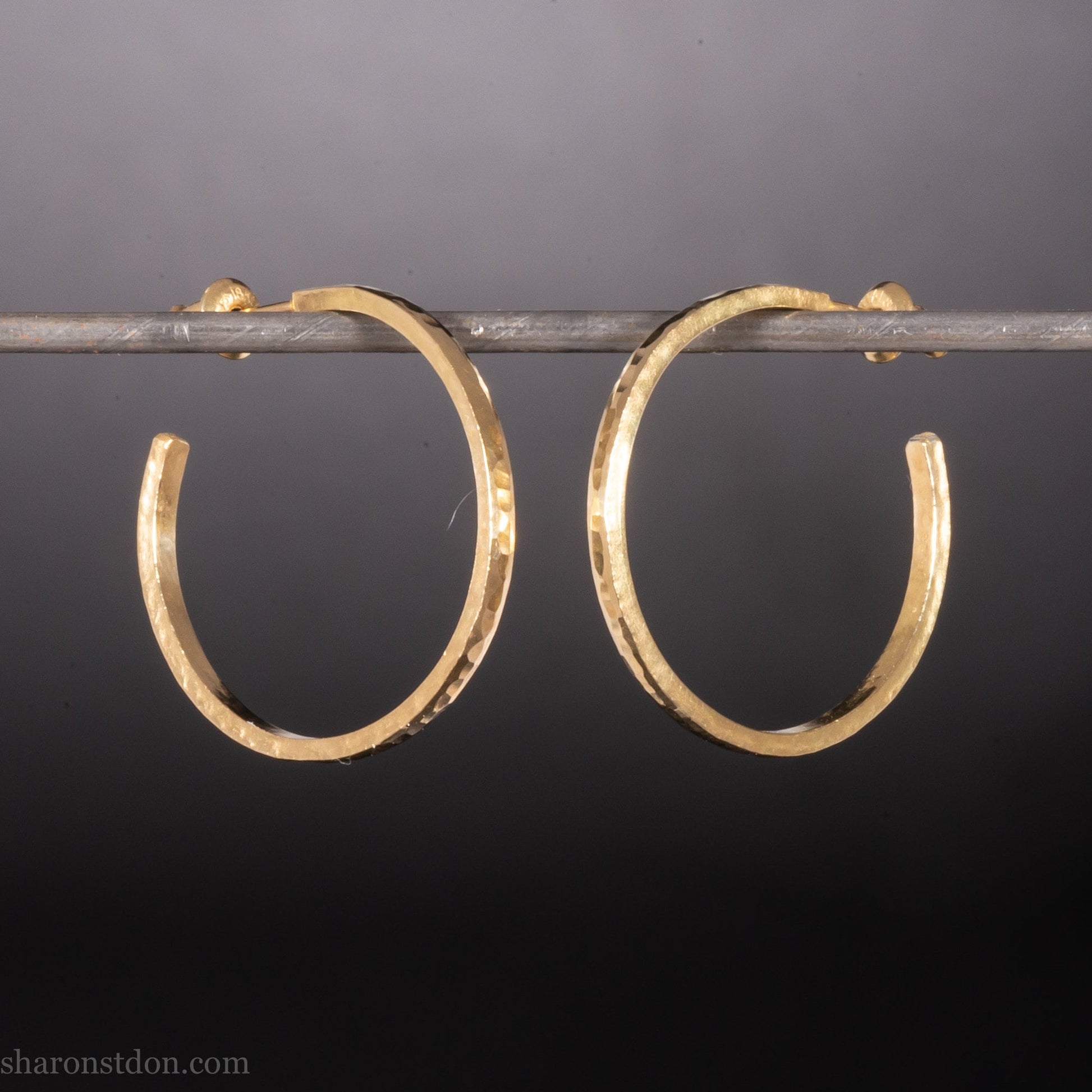 25mm diameter by 1.5mm thick handmade solid 14k yellow gold hoop earrings with solid 14k gold posts and backs. Handmade by Sharon SaintDon in North America. Hammered from solid gold with a matte finish.