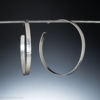 Large, solid sterling silver hoop earrings. Handmade in North America by Sharon SaintDon. 50mm diameter x 5mm wide, .75mm thick. Hammered, wavy, texture with a matte brushed finish, silver posts and backs.