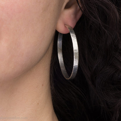 Large, solid sterling silver hoop earrings. Handmade in North America by Sharon SaintDon. 50mm diameter x 5mm wide, .75mm thick. Hammered, wavy, texture with a matte brushed finish, silver posts and backs.