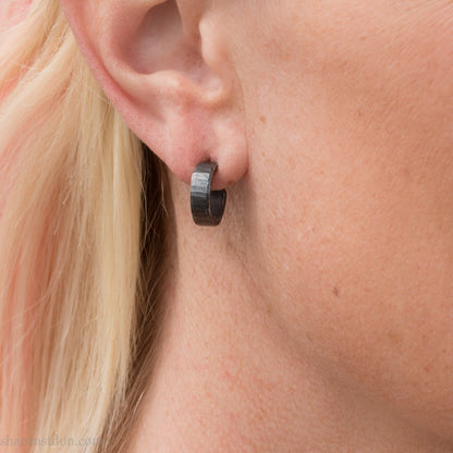 Close up photo of a woman wearing oxidized black 14mm x 4mm hammered solid sterling silver hoop earrings.