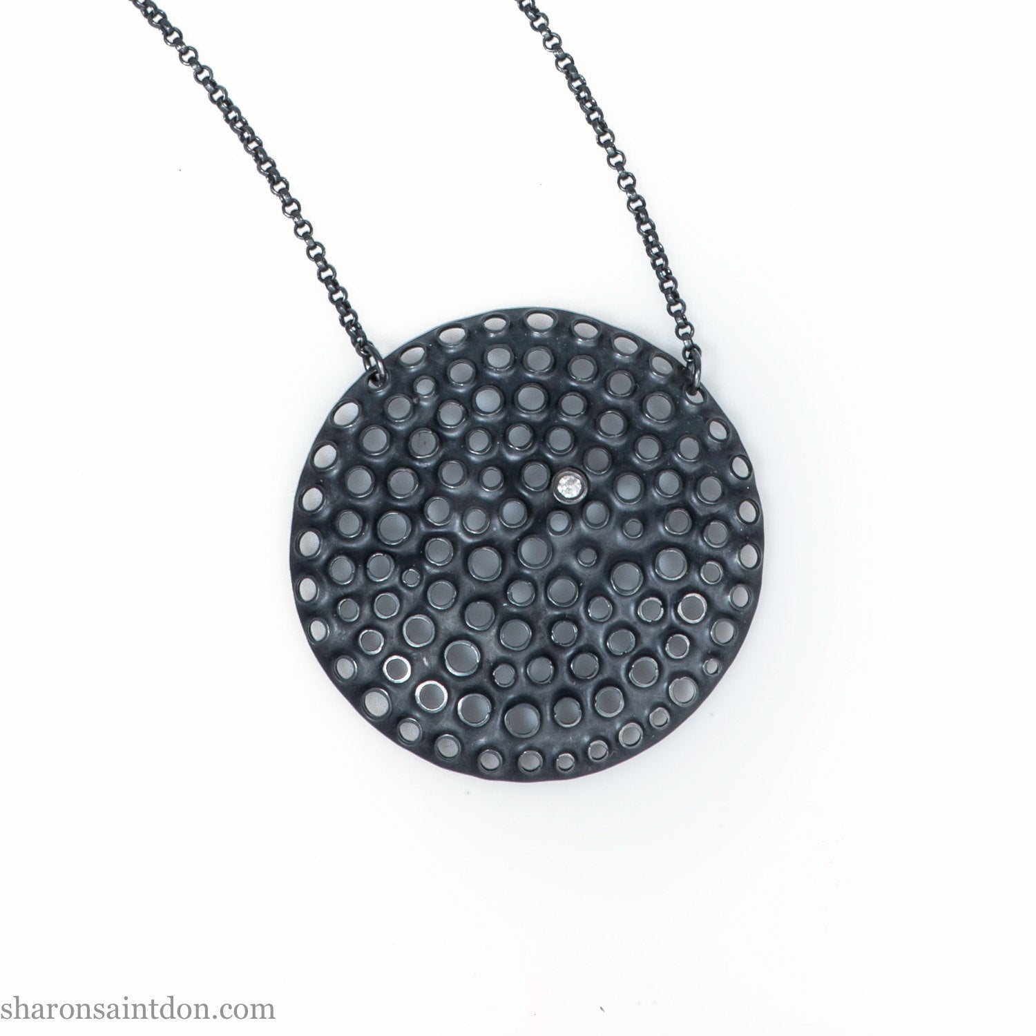 Large round, handcrafted sterling silver pendant necklace with perforated holes and oxidized black finish, accented with cubic zirconia, on black chain.