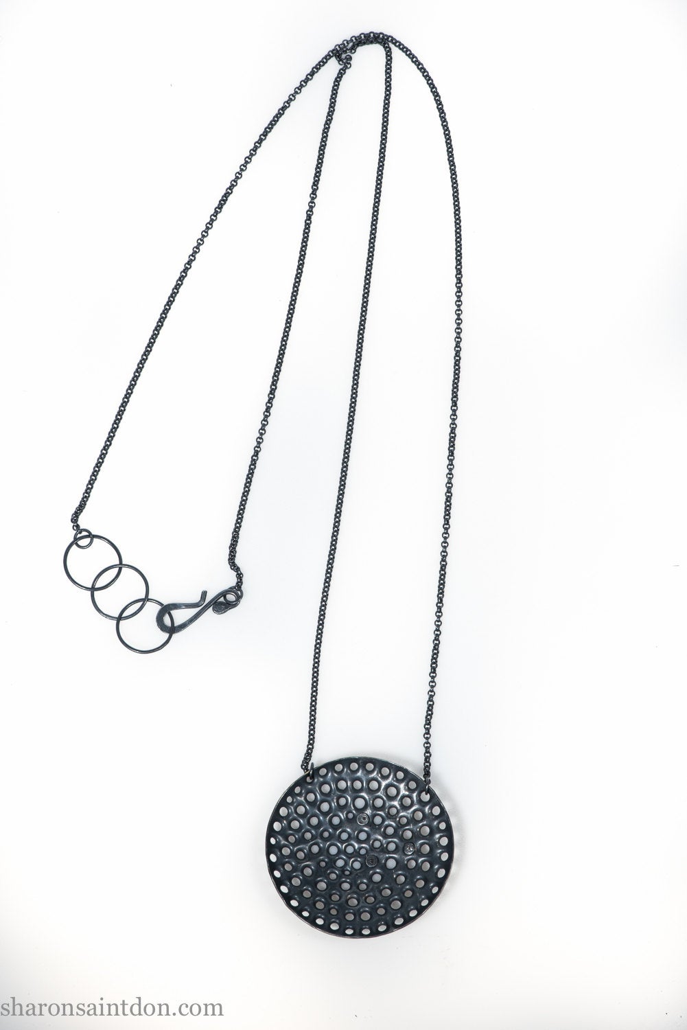 Large round, handcrafted sterling silver pendant necklace with perforated holes and oxidized black finish, accented with cubic zirconia, on black chain. 