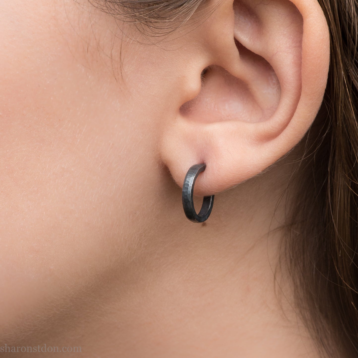 Hand hammered solid 925 sterling silver hoop earrings, oxidized black, 14mm diameter x 2mm wide, worn on an ear.
