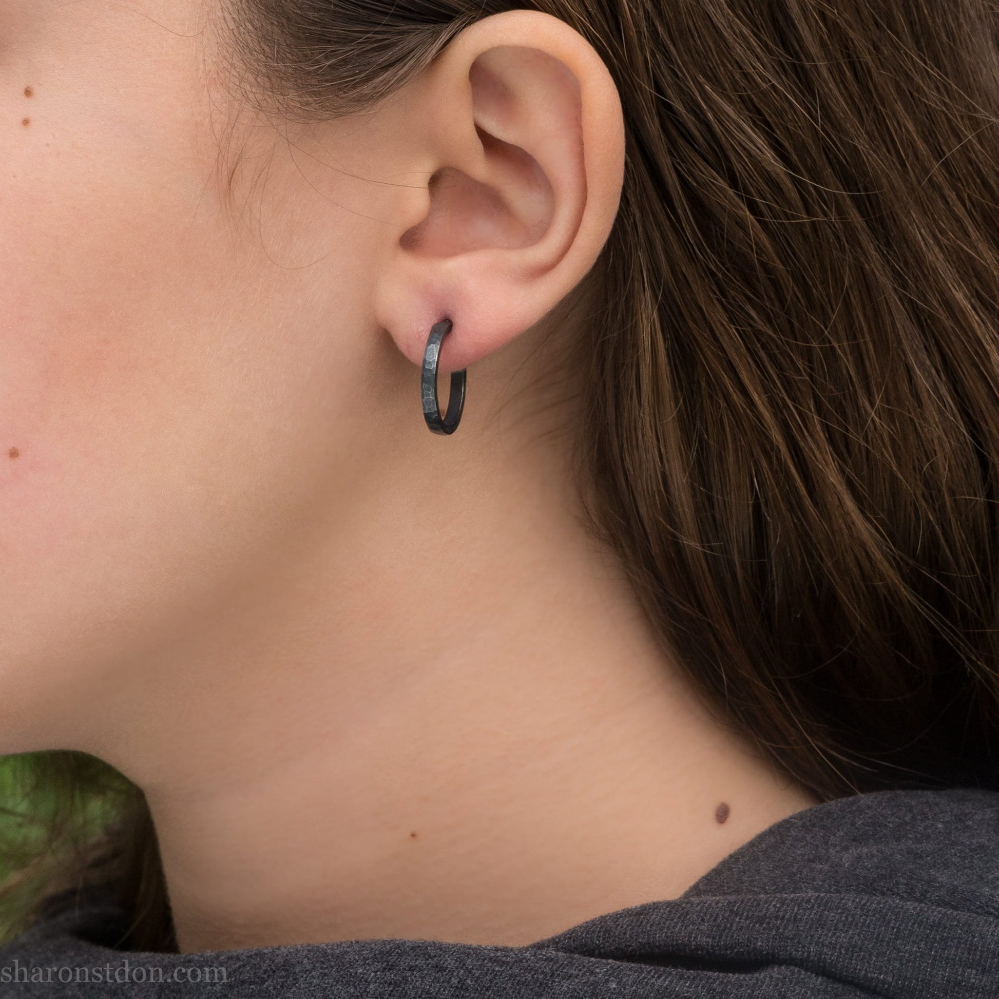 Oxidized black sterling silver 18x2mm hammered hoop earrings worn on ear by woman, side profile.