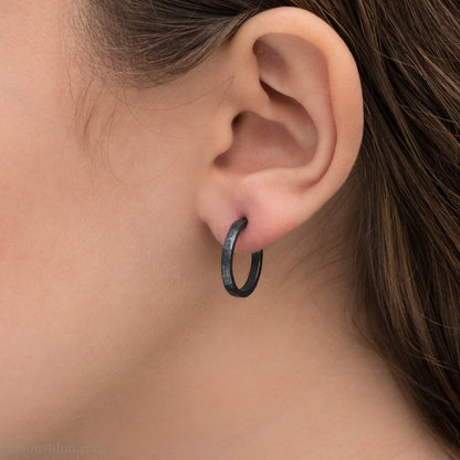 Oxidized black sterling silver 18x2mm hammered hoop earrings worn on ear by woman, side profile.