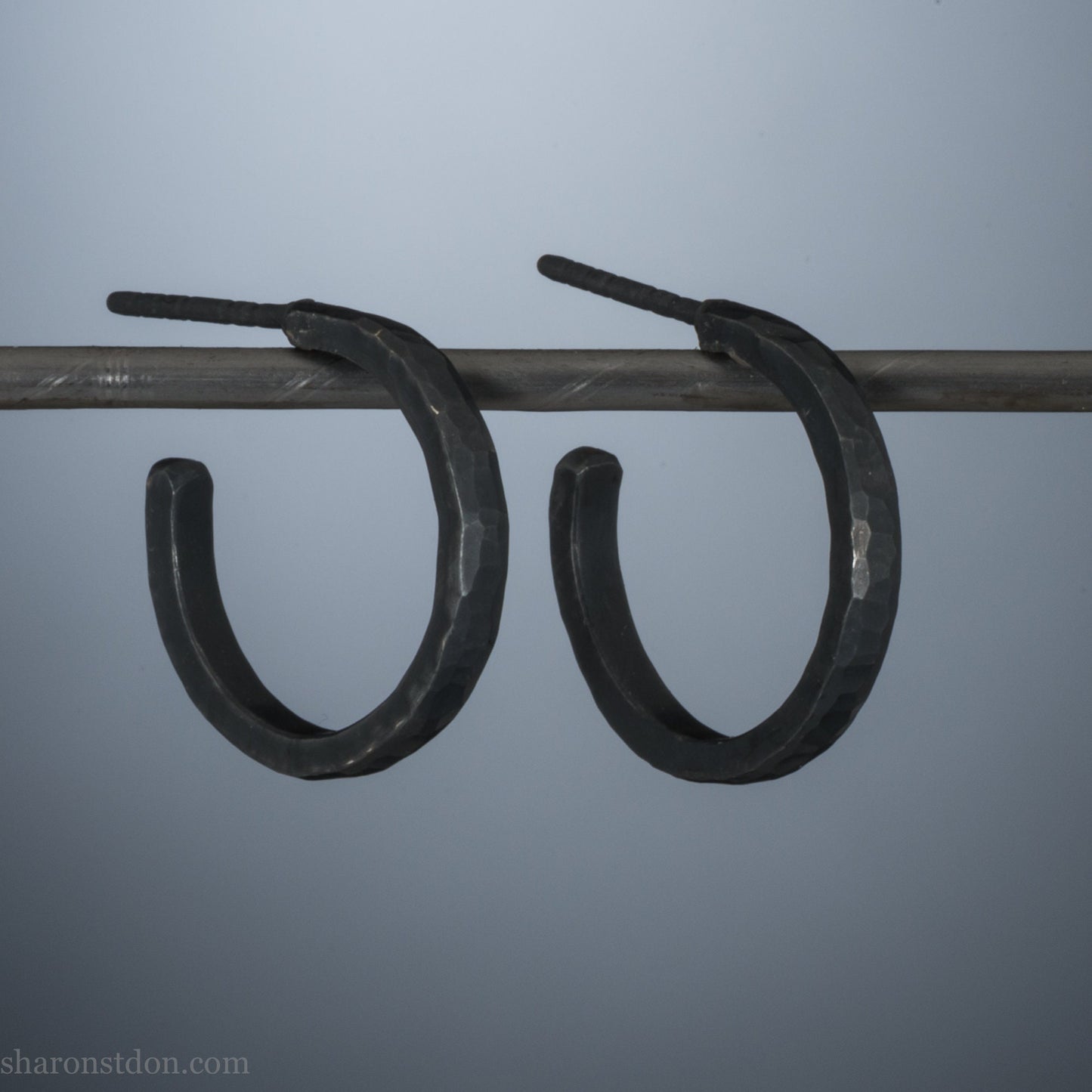 18x2mm oxidized black 925 sterling silver hammered hoop earrings with a matte dark patina, shown on display bar.