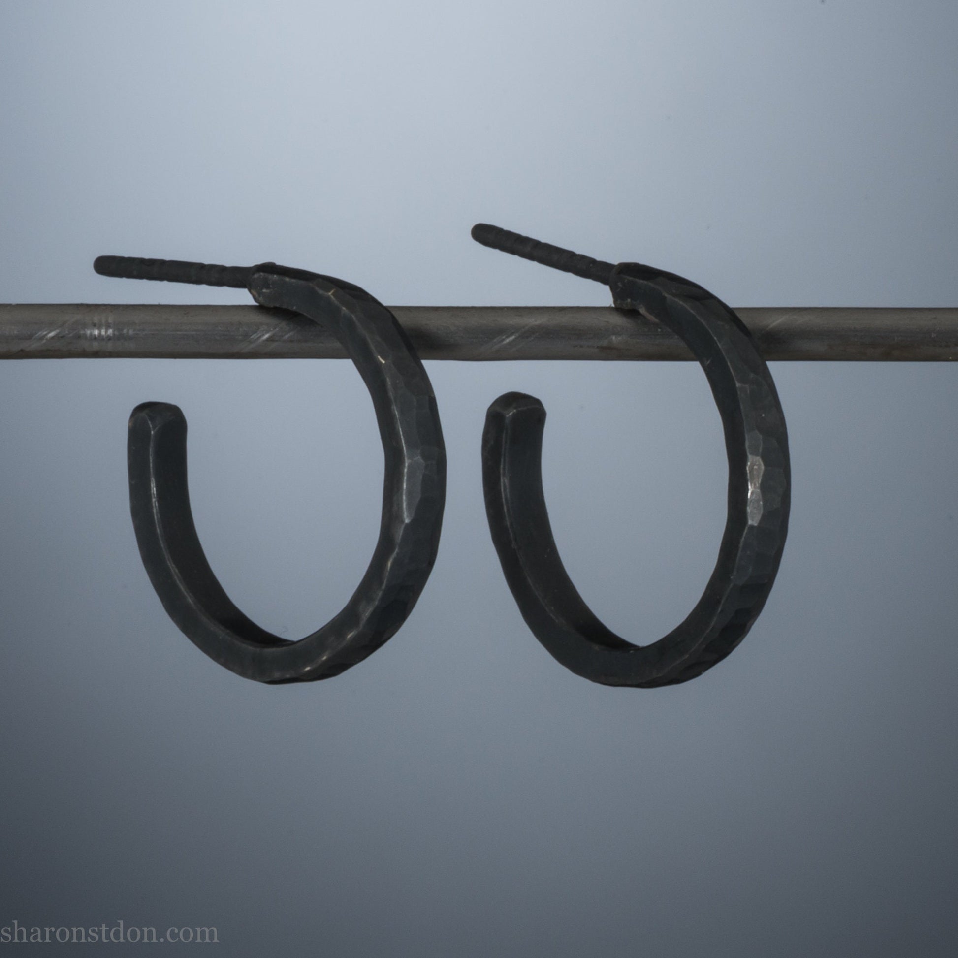 18x2mm oxidized black 925 sterling silver hammered hoop earrings with a matte dark patina, shown on display bar.