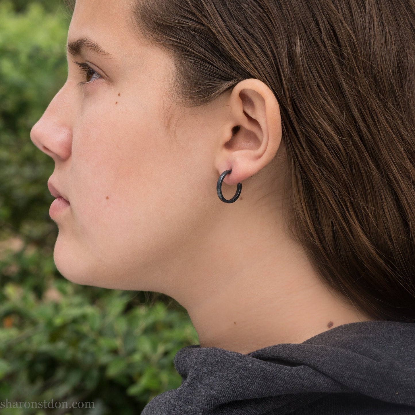 Oxidized black sterling silver 18x2mm hammered hoop earrings worn on ear by woman, side profile.
