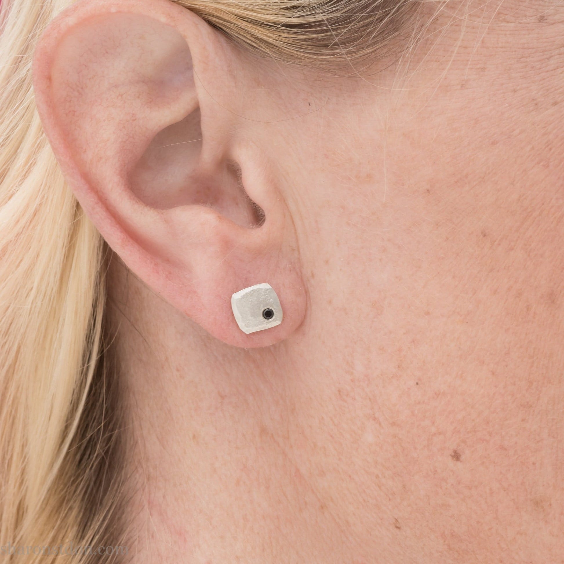 Black spinel stud earrings in sterling silver, 7mm square with matte finish, worn on a human ear.