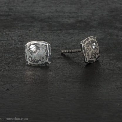 7mm square 925 sterling silver stud earrings with an imitation diamond gemstone in the corner. Hammered texture with an antiqued, oxidized black finish rubbed back to show the texture. Handmade by Sharon SaintDon in North America for men or women.