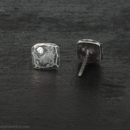 7mm square 925 sterling silver stud earrings with an imitation diamond gemstone in the corner. Hammered texture with an antiqued, oxidized black finish rubbed back to show the texture. Handmade by Sharon SaintDon in North America for men or women.