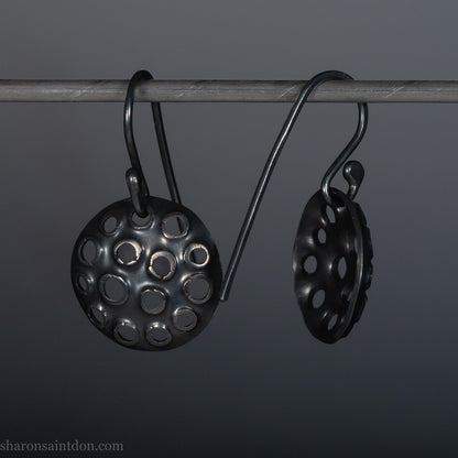 15mm round 925 sterling silver disc earrings with mesh perforated holes. Handmade solid oxidized black silver dangle earrings by Sharon SaintDon in North America with hand made black silver french ear hooks.