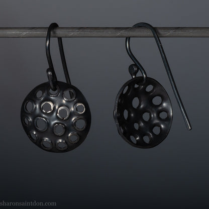 15mm round 925 sterling silver disc earrings with mesh perforated holes. Handmade solid oxidized black silver dangle earrings by Sharon SaintDon in North America with hand made black silver french ear hooks.