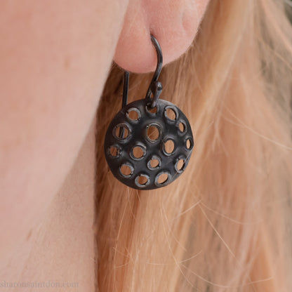 15mm round 925 sterling silver disc earrings with mesh perforated holes. Handmade solid oxidized black silver dangle earrings by Sharon SaintDon in North America with hand made black silver french ear hooks.