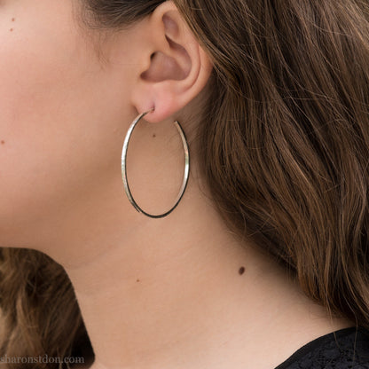 Solid 925 sterling silver hoop earrings. 50mm diameter, 2mm wide, 1.5mm thick with a matte, shiny finish. Lightweight hammered large hoop earrings handmade by Sharon SaintDon in North America.