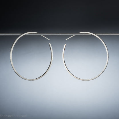 Solid 925 sterling silver hoop earrings. 50mm diameter, 2mm wide, 1.5mm thick with a matte, shiny finish. Lightweight hammered large hoop earrings handmade by Sharon SaintDon in North America.