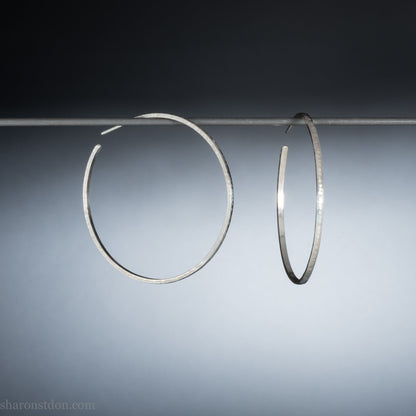 Solid 925 sterling silver hoop earrings. 50mm diameter, 2mm wide, 1.5mm thick with a matte, shiny finish. Lightweight hammered large hoop earrings handmade by Sharon SaintDon in North America.