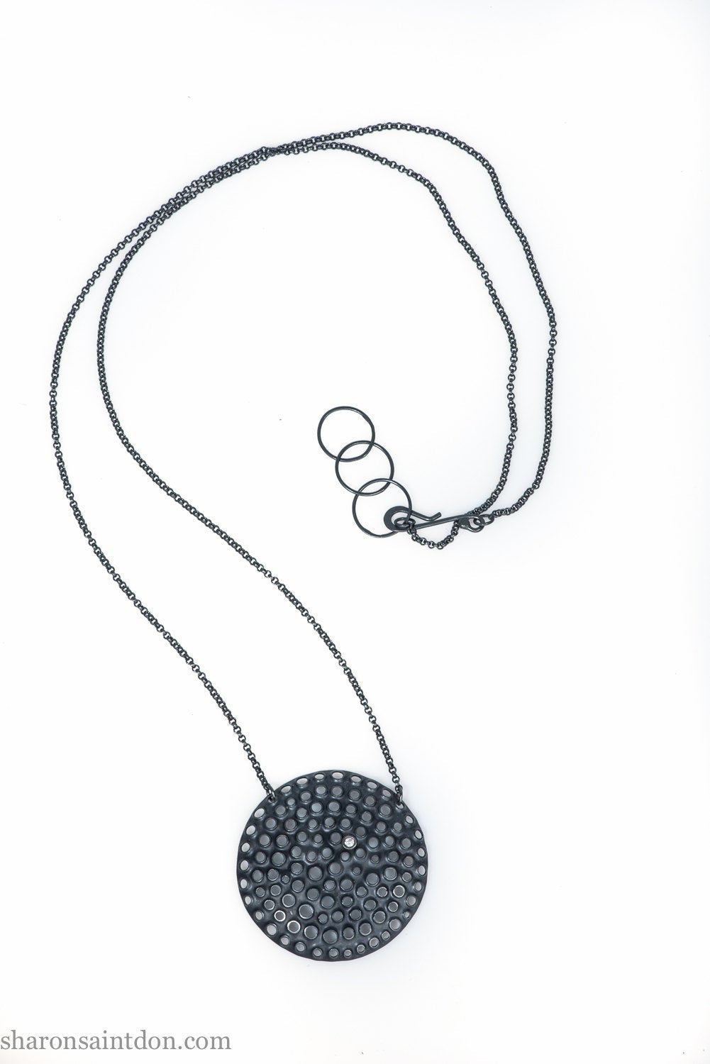 Handmade, large, 925 sterling silver pendant necklace by Sharon SaintDon. 50mm diameter round, covered in perforated holes, oxidized black with cubic zirconia gemstone. 36 or 18 inch black chain.