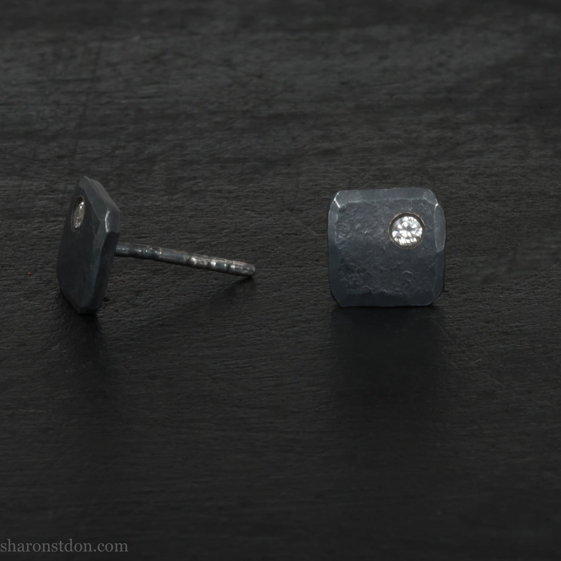 7mm square 925 sterling silver stud earrings with an imitation diamond gemstone in the corner. Hammered texture with a matte, charcoal, oxidized black finish. Handmade by Sharon SaintDon in North America for men or women.