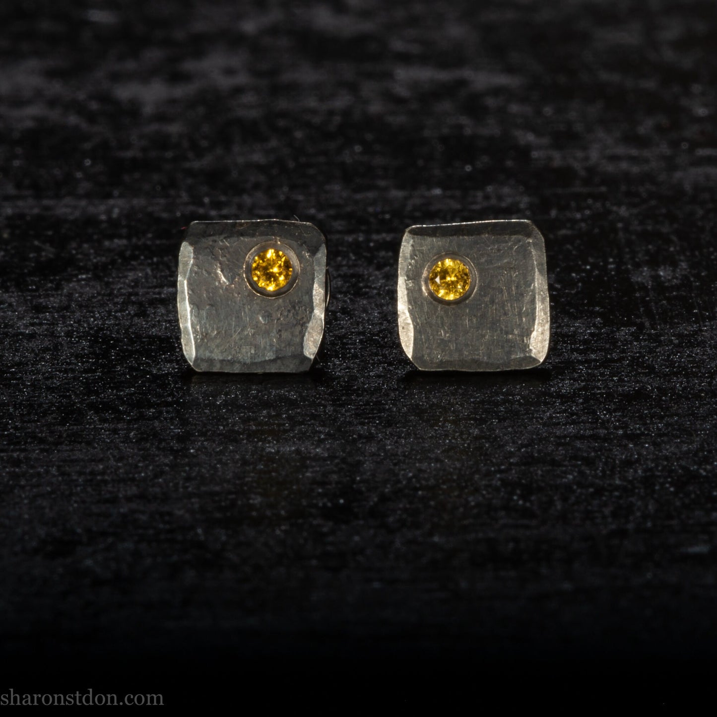 Handmade 925 sterling silver stud earrings handmade by Sharon SaintDon In North America. 7mm x 7mm hammered, square, oxidized black silver with a golden yellow topaz gemstone in the corner.