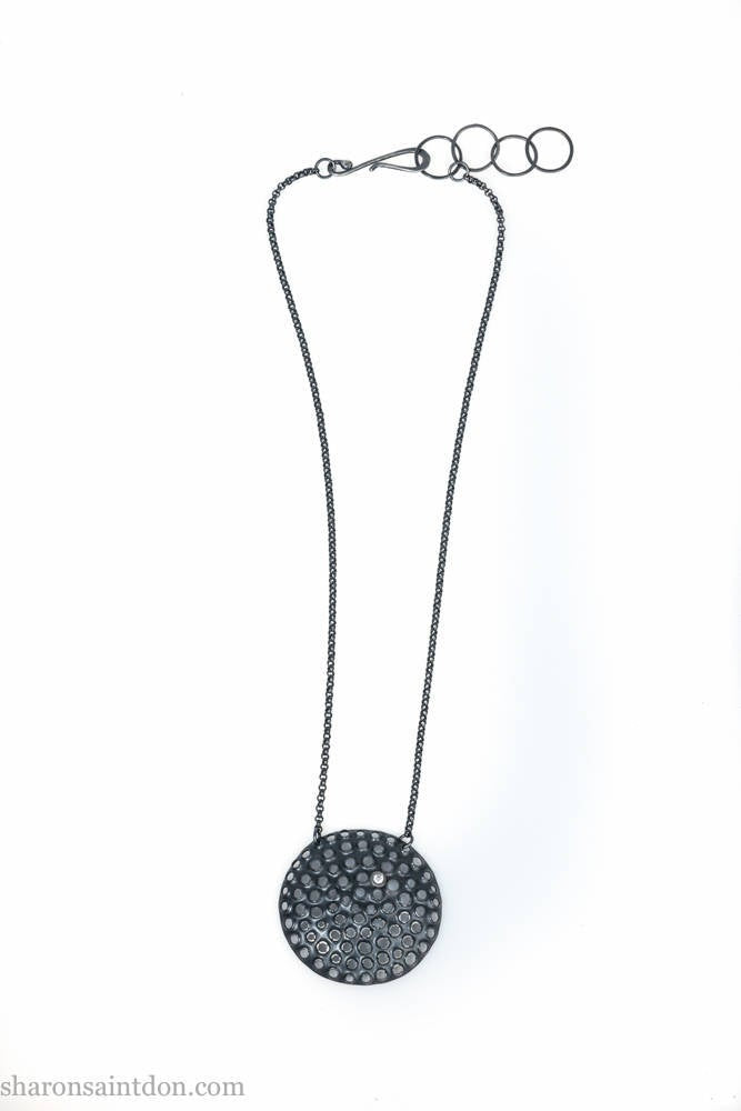 Handmade, large, 925 sterling silver pendant necklace by Sharon SaintDon. 50mm diameter round, covered in perforated holes, oxidized black with cubic zirconia gemstone. 36 or 18 inch black chain.