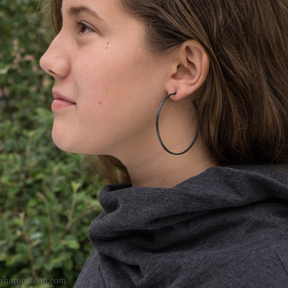 Handmade 925 sterling silver hoop earrings for women. 55mm diameter, 2mm wide, oxidized black, large hoops for daily wear. Minimalist, comfortable, lightweight with a hammered, texture.