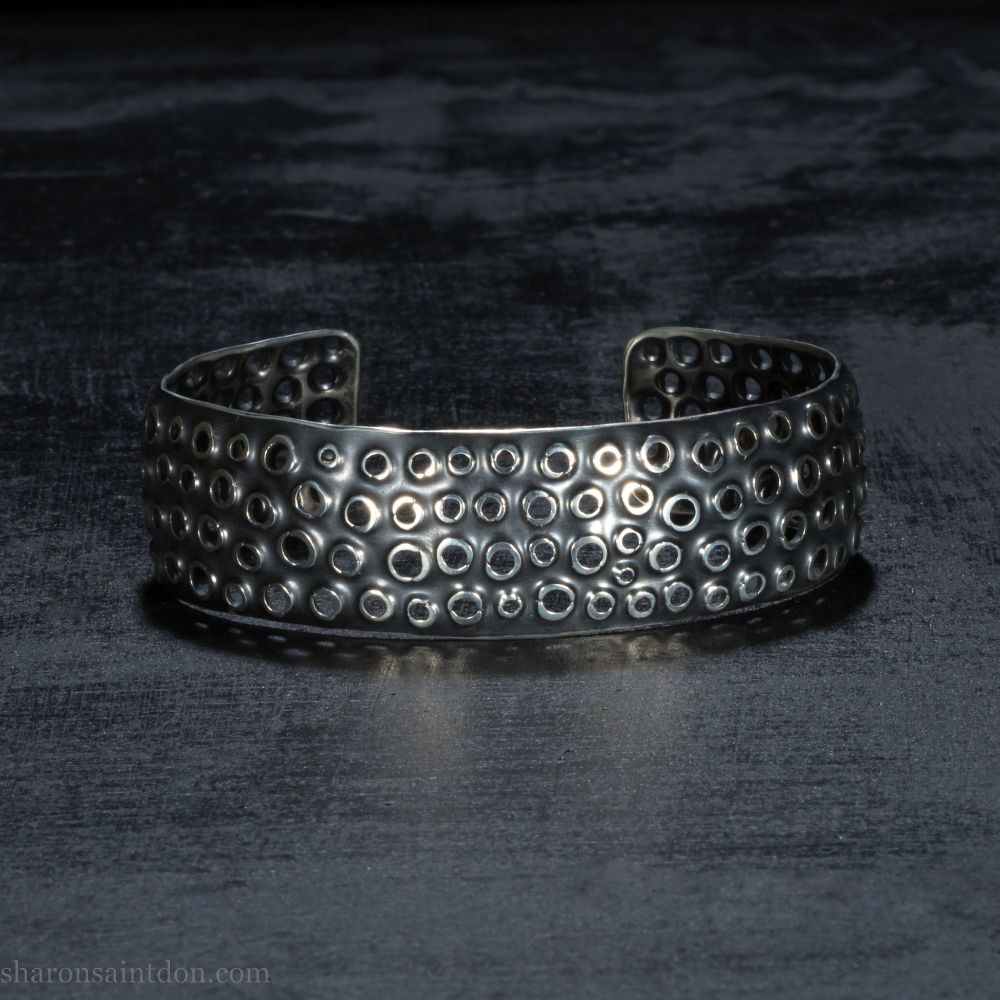 925 sterling silver cuff bracelet handmade in USA. 2cm wide, 40cm x 60cm oval with approximately 28mm flexible opening for wrist. Punched perforated hole texture, oxidized black and rubbed back to show circles as white shiny silver.
