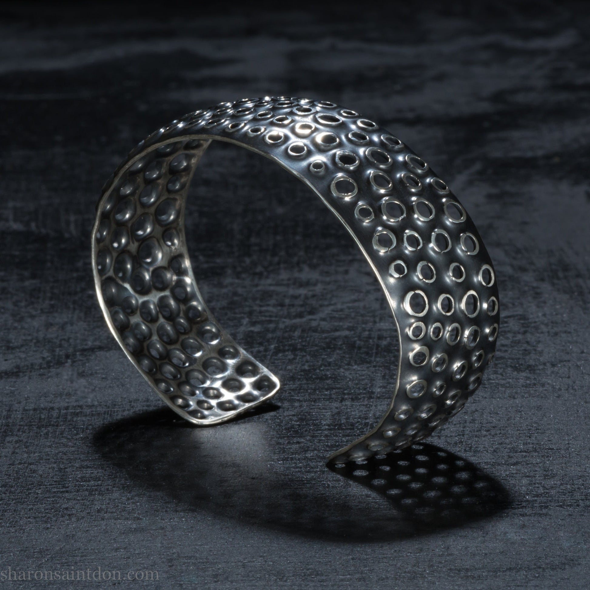 925 sterling silver cuff bracelet handmade in USA. 2cm wide, 40cm x 60cm oval with approximately 28mm flexible opening for wrist. Punched perforated hole texture, oxidized black and rubbed back to show circles as white shiny silver.