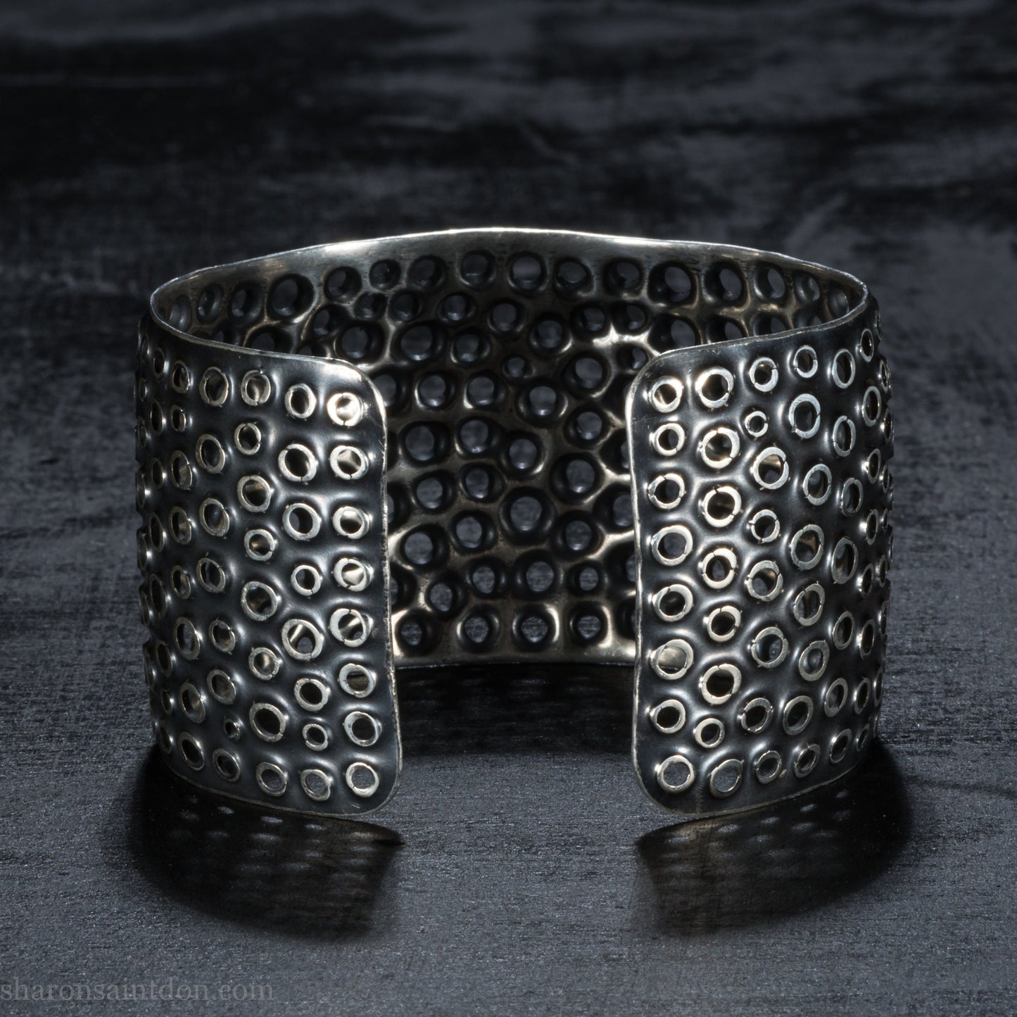 925 sterling silver cuff bracelet handmade in USA. 4cm wide, 40cm x 60cm oval with approximately 28mm flexible opening for wrist. Punched perforated hole texture, oxidized black and rubbed back to show circles as white shiny silver.