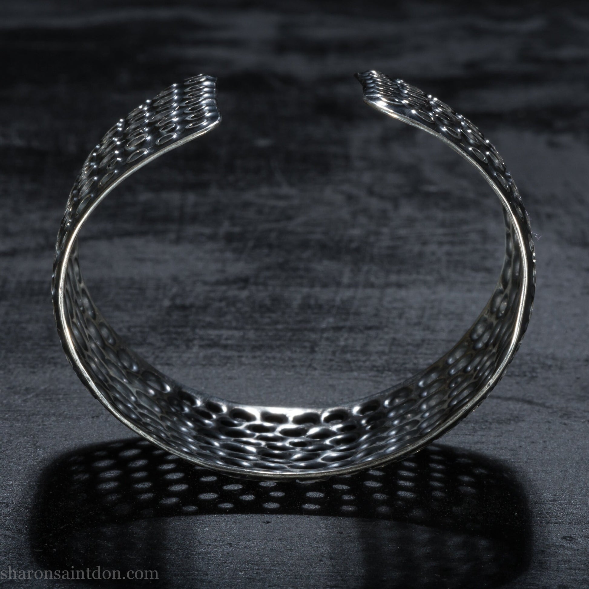 925 sterling silver cuff bracelet handmade in USA. 4cm wide, 40cm x 60cm oval with approximately 28mm flexible opening for wrist. Punched perforated hole texture, oxidized black and rubbed back to show circles as white shiny silver.