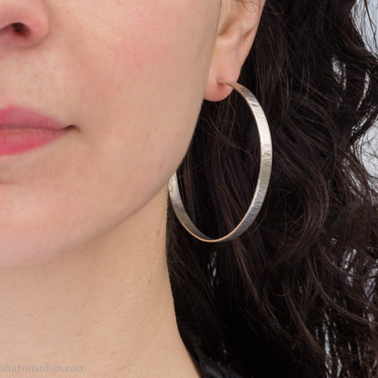 Woman wearing large hammered solid sterling silver hoop earrings 55mm diameter 5mm wide