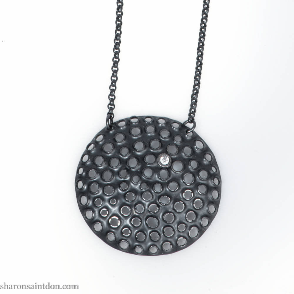 Large round, handcrafted sterling silver pendant necklace with perforated holes and oxidized black finish, accented with cubic zirconia, on black chain.