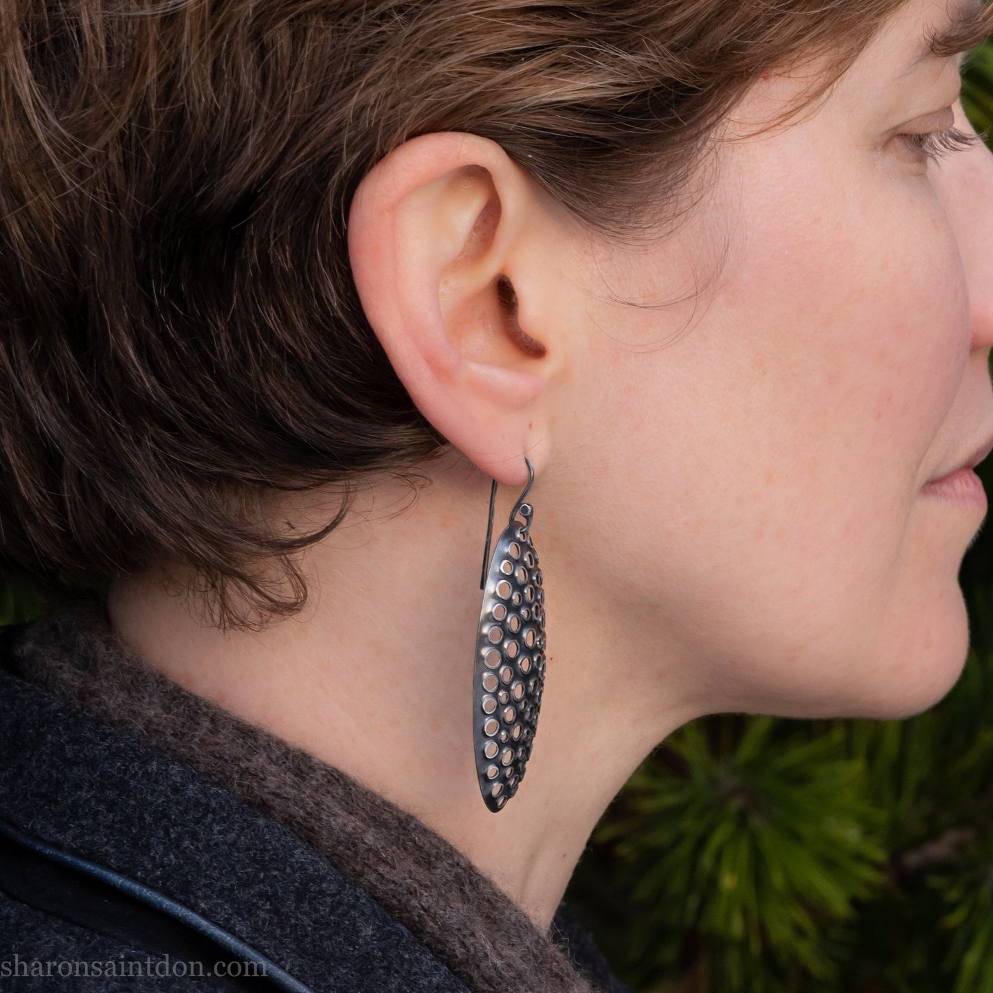 Large oval sterling silver dangle earrings with hand-punched detailed holes and antiqued finish, worn on ear.