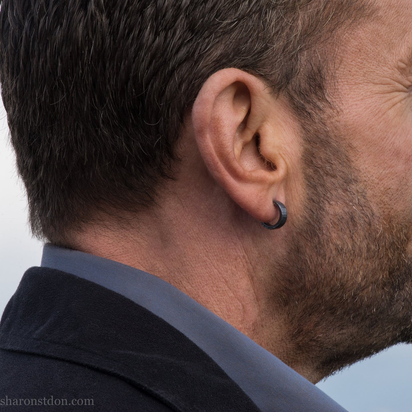 Close up photo of a man wearing handcrafted oxidized black 14mm x 4mm hammered solid sterling silver hoop earrings.
