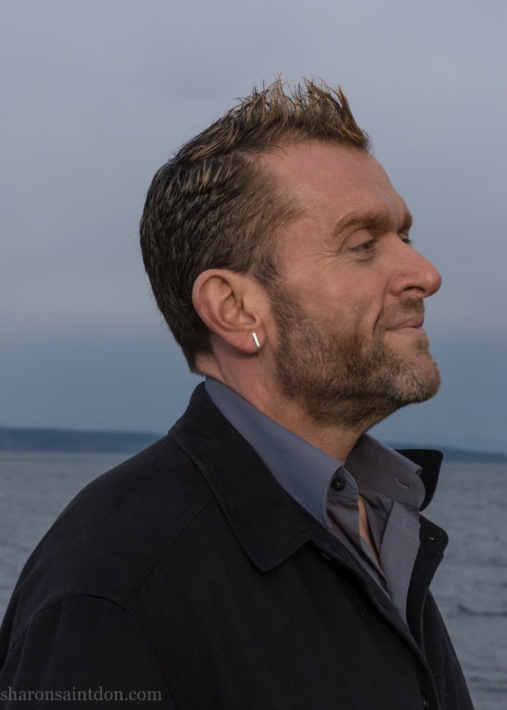 Men's solid 925 sterling silver J wrap huggie hoop earrings, matte finish, handcrafted. Worn on ear of man with beard.