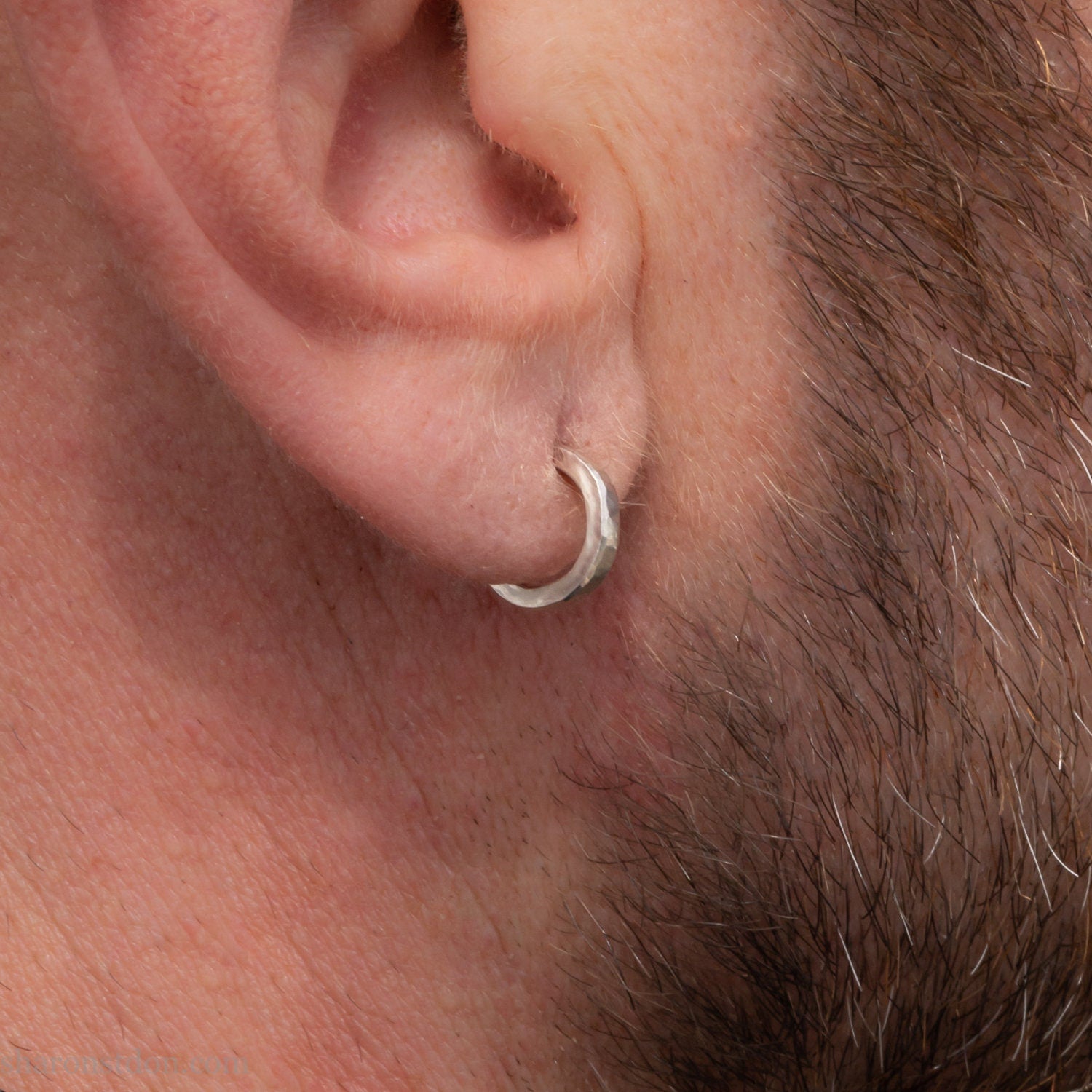 Handmade solid sterling silver hoop earrings, hammered by hand with a matte, brushed, shiny finish. SIZE: 12mm exterior diameter, 9mm interior, 2mm wide. and 1.5mm thick. Pictured on a man with light skin and brown beard.
