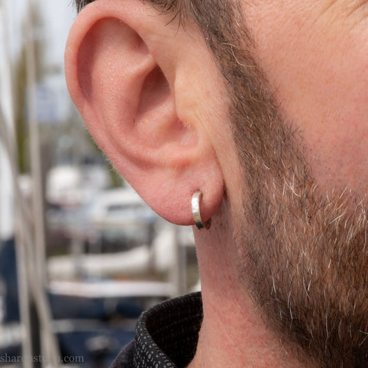 Handmade solid sterling silver hoop earrings, hammered by hand with a matte, brushed, shiny finish. SIZE: 12mm exterior diameter, 9mm interior, 2mm wide. and 1.5mm thick. Pictured on a man with light skin and brown beard.