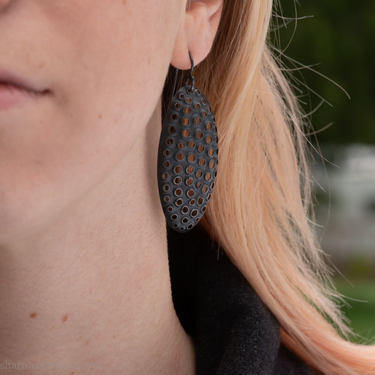 Woman wearing oxidized silver dangle earrings with hand-punched oval apertures, 50mm long.