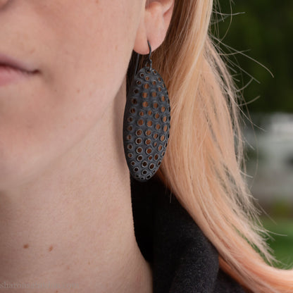 Woman wearing oxidized silver dangle earrings with hand-punched oval apertures, 50mm long.