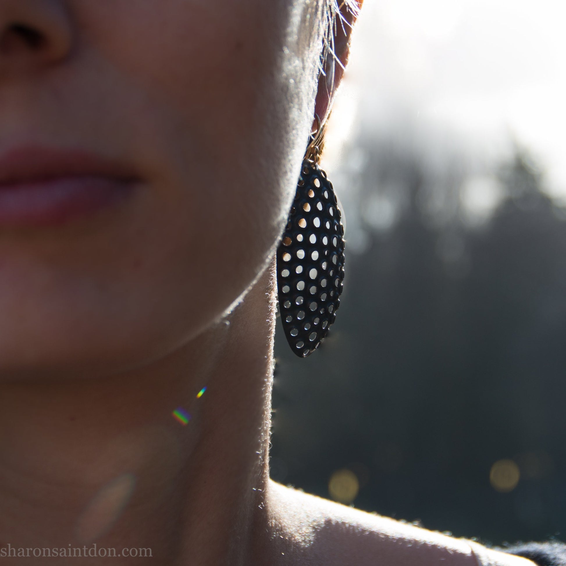 Woman wearing oxidized silver dangle earrings with hand-punched oval apertures, 50mm long.