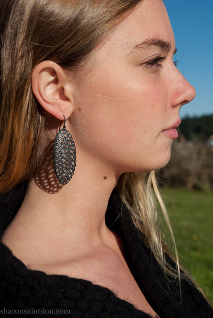 Woman wearing oxidized silver dangle earrings with hand-punched oval apertures, 50mm long.