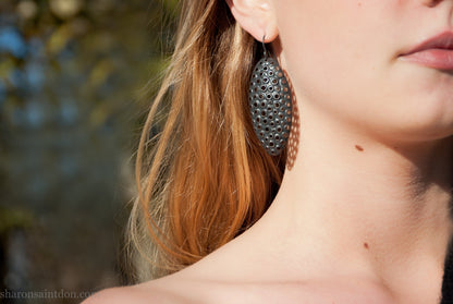 Woman wearing oxidized silver dangle earrings with hand-punched oval apertures, 50mm long.