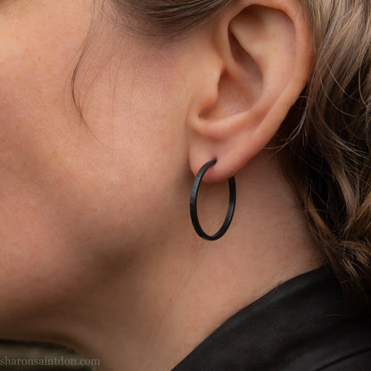 25mm oxidized black sterling silver round hammered hoop earring, close-up on model’s ear.