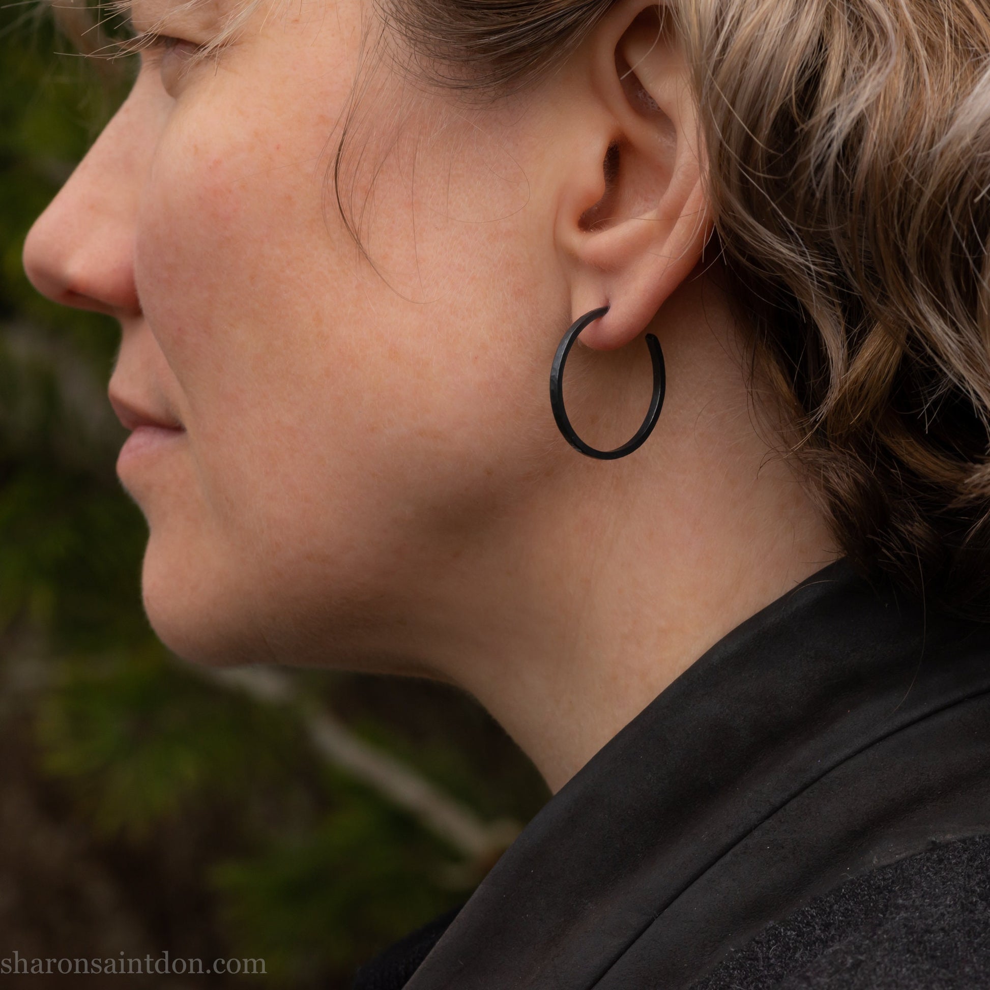 25mm oxidized black sterling silver round hammered hoop earring, close-up on model’s ear.