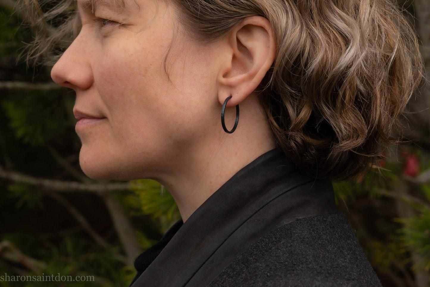 25mm oxidized black sterling silver round hammered hoop earring, close-up on model’s ear.