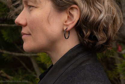 25mm oxidized black sterling silver round hammered hoop earring, close-up on model’s ear.